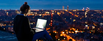 person sitting on hillside using laptop