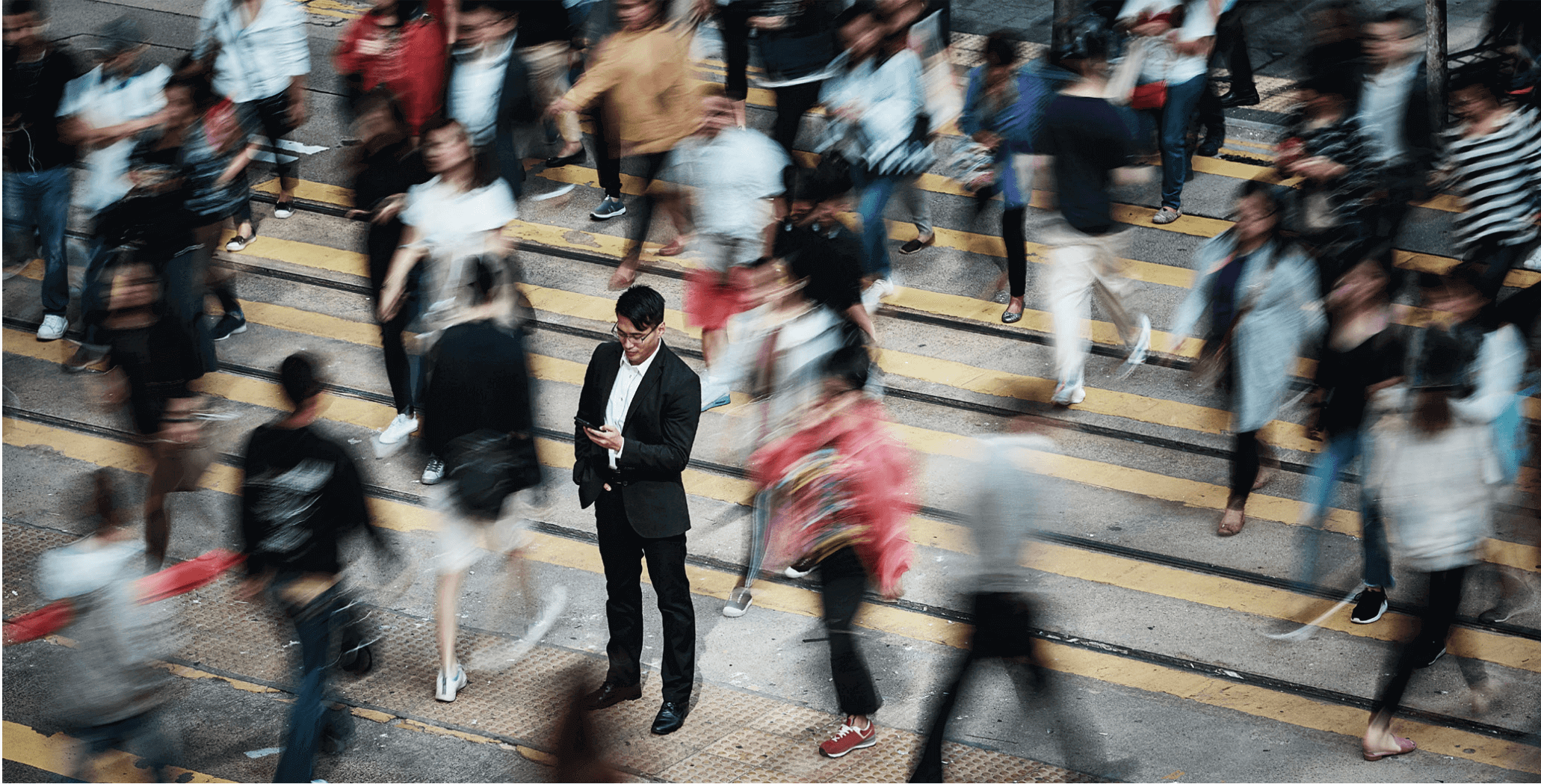 A man standing still on a busy crosswalk while crowds blur past him.
