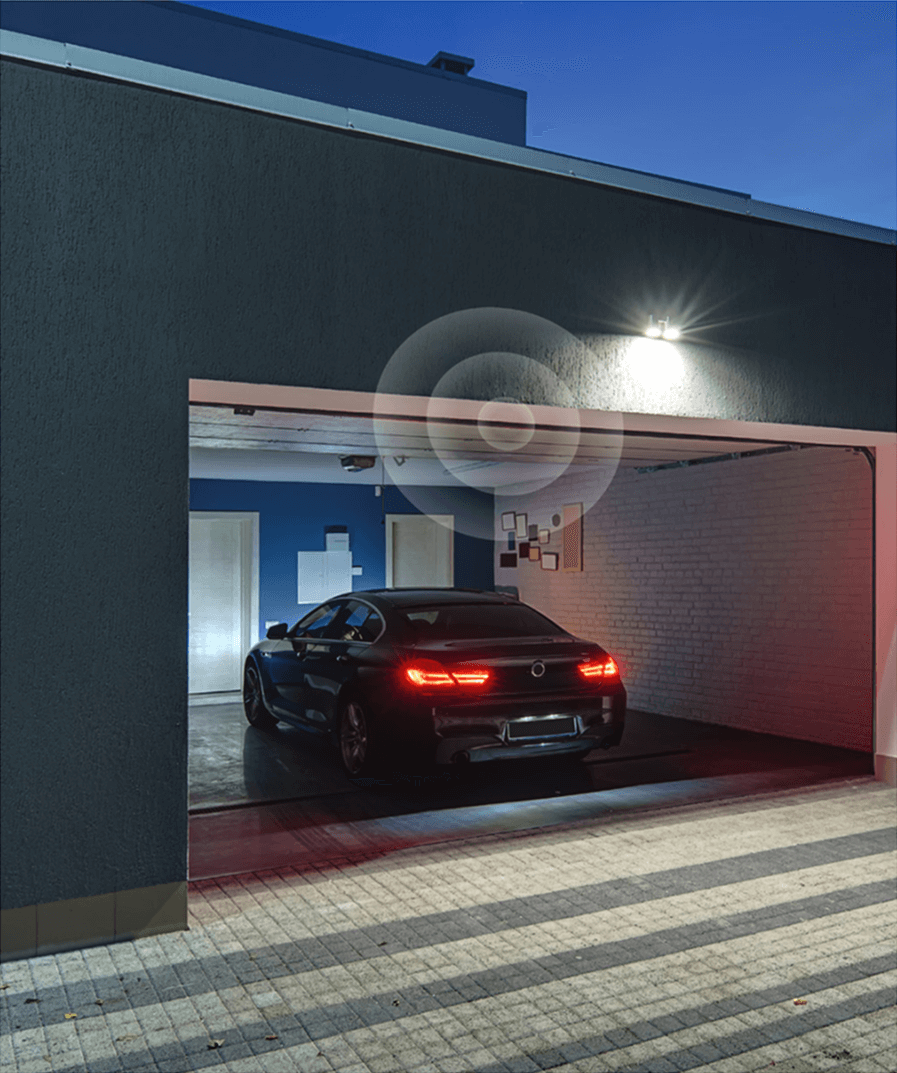 A black car parked in a modern, open garage at dusk with tail lights on.